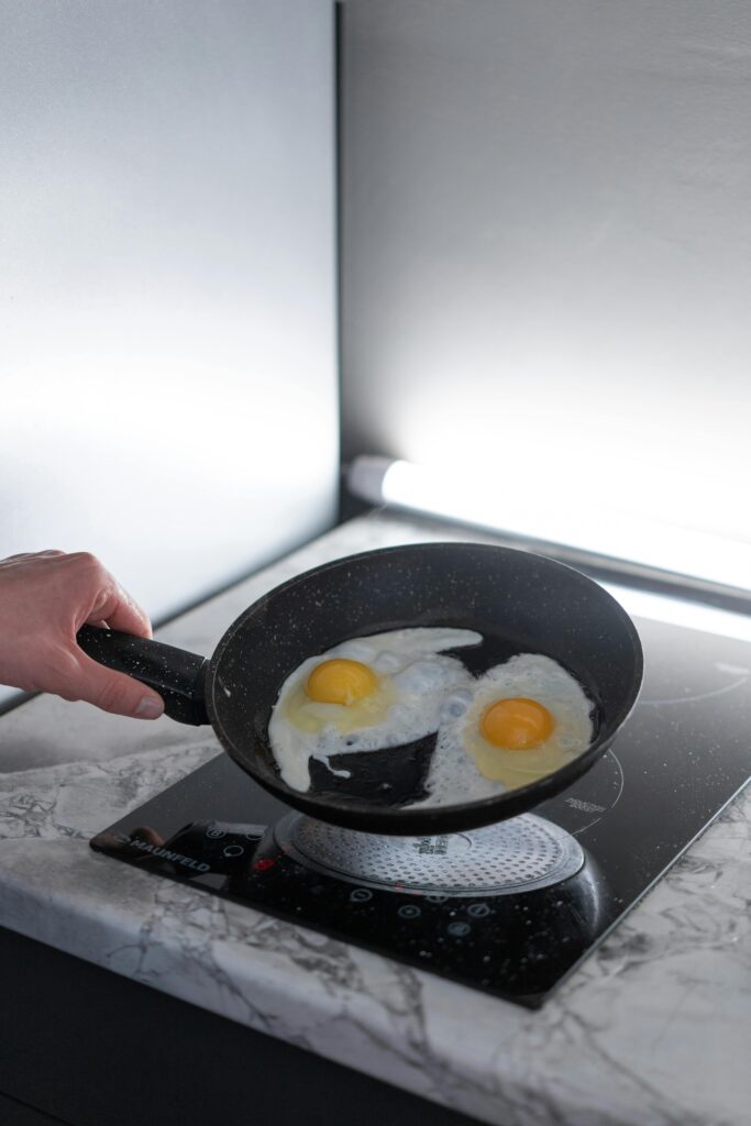 A person frying two eggs in a non-stick pan on an induction stove in a modern kitchen.