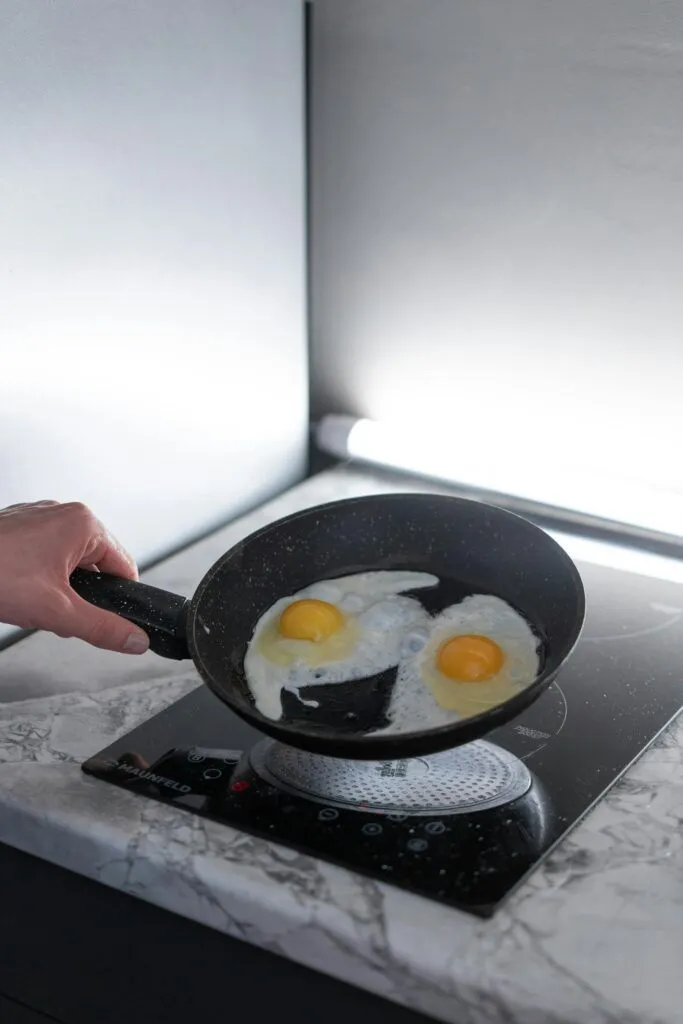 A person frying two eggs in a non-stick pan on an induction stove in a modern kitchen.