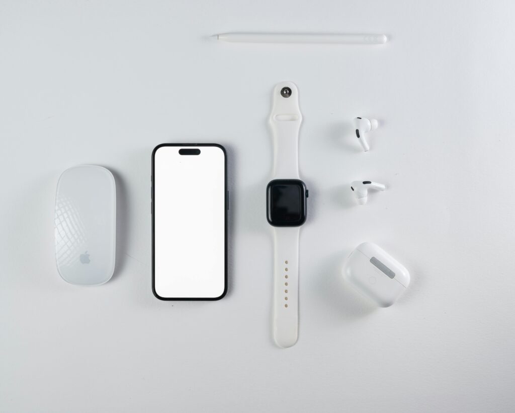 Minimalist flat lay of smartphone, smartwatch, wireless earbuds, and mouse on a white background.