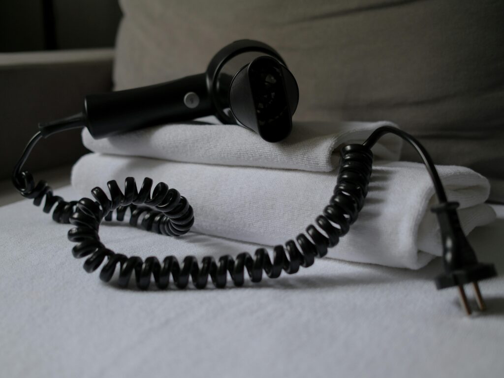 A coiled hair dryer placed on folded white towels, suggesting a hotel setting.