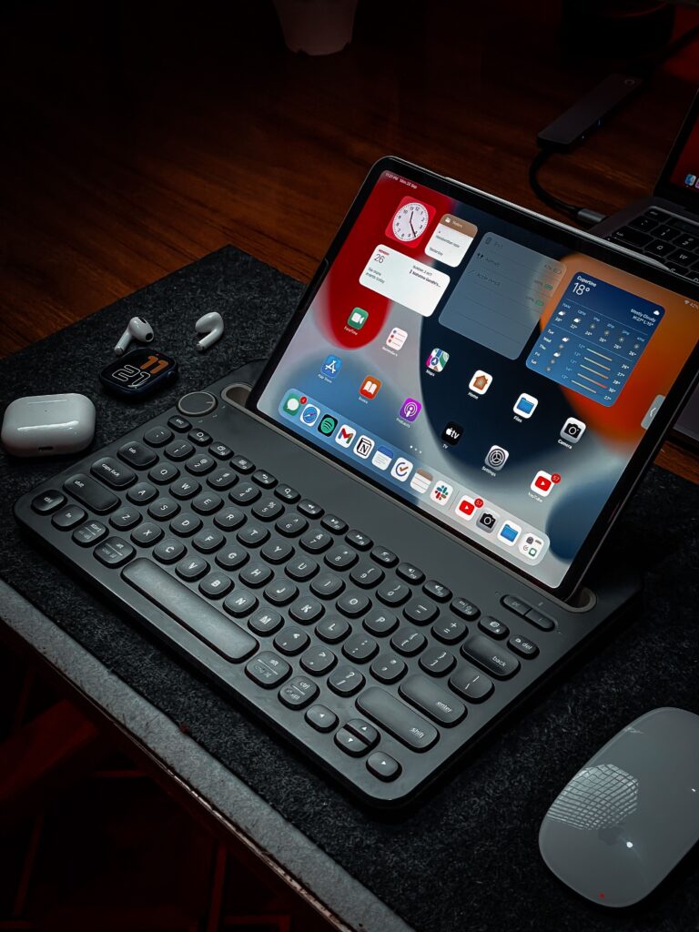 Close-up of a digital workspace featuring a tablet, keyboard, mouse, and wireless earbuds.
