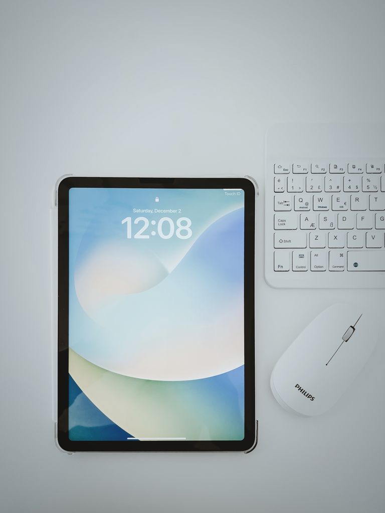 Top view of a modern workspace with a tablet, keyboard, and mouse on a white surface.